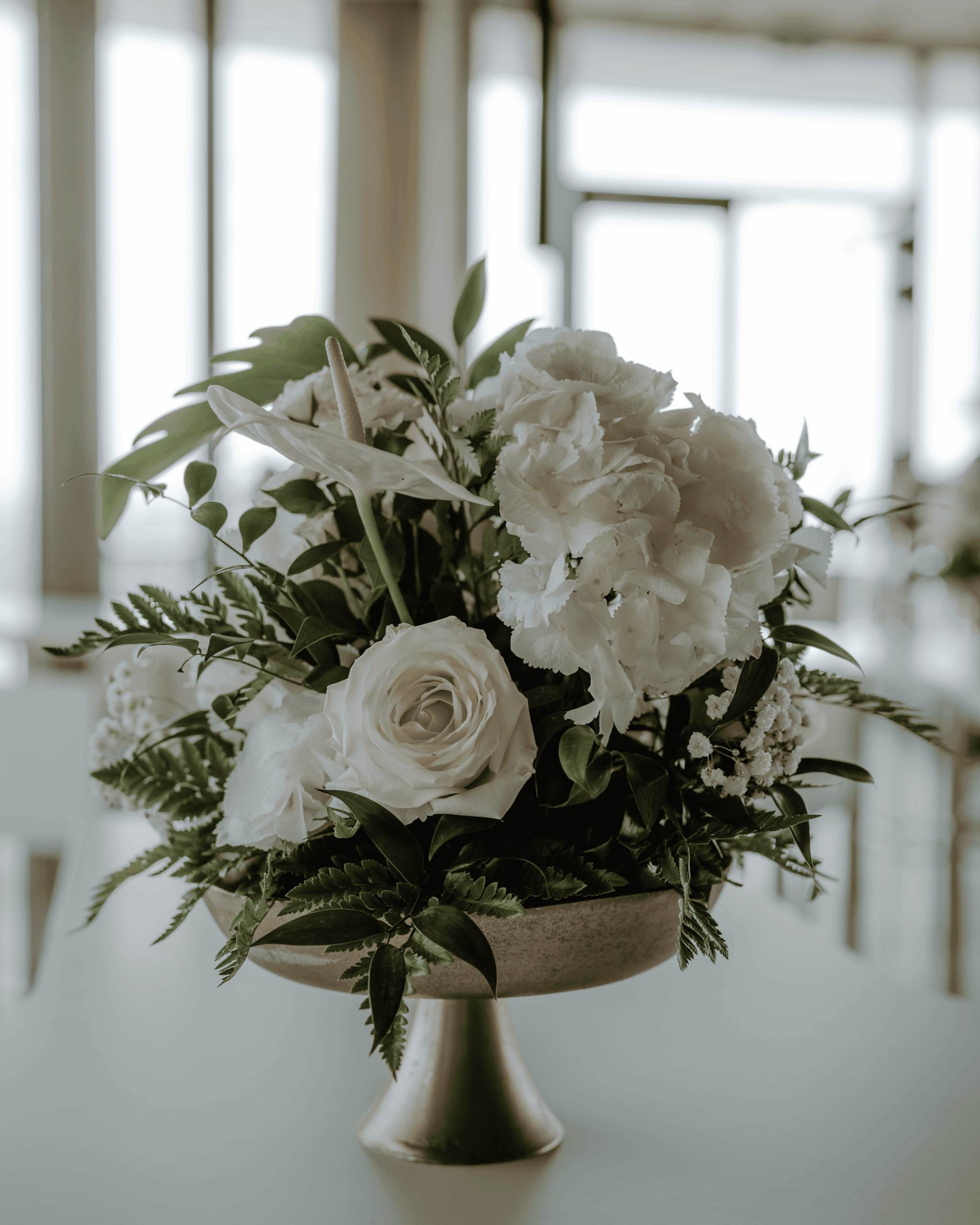 Florales Tischarrangement mit weißen Rosen und grünen Blättern in eleganter Vase