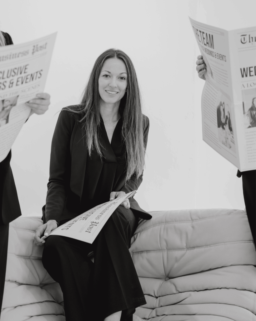 Hochzeitsplanerin sitzt entspannt auf Sofa und hält stilisierte Hochzeitszeitung