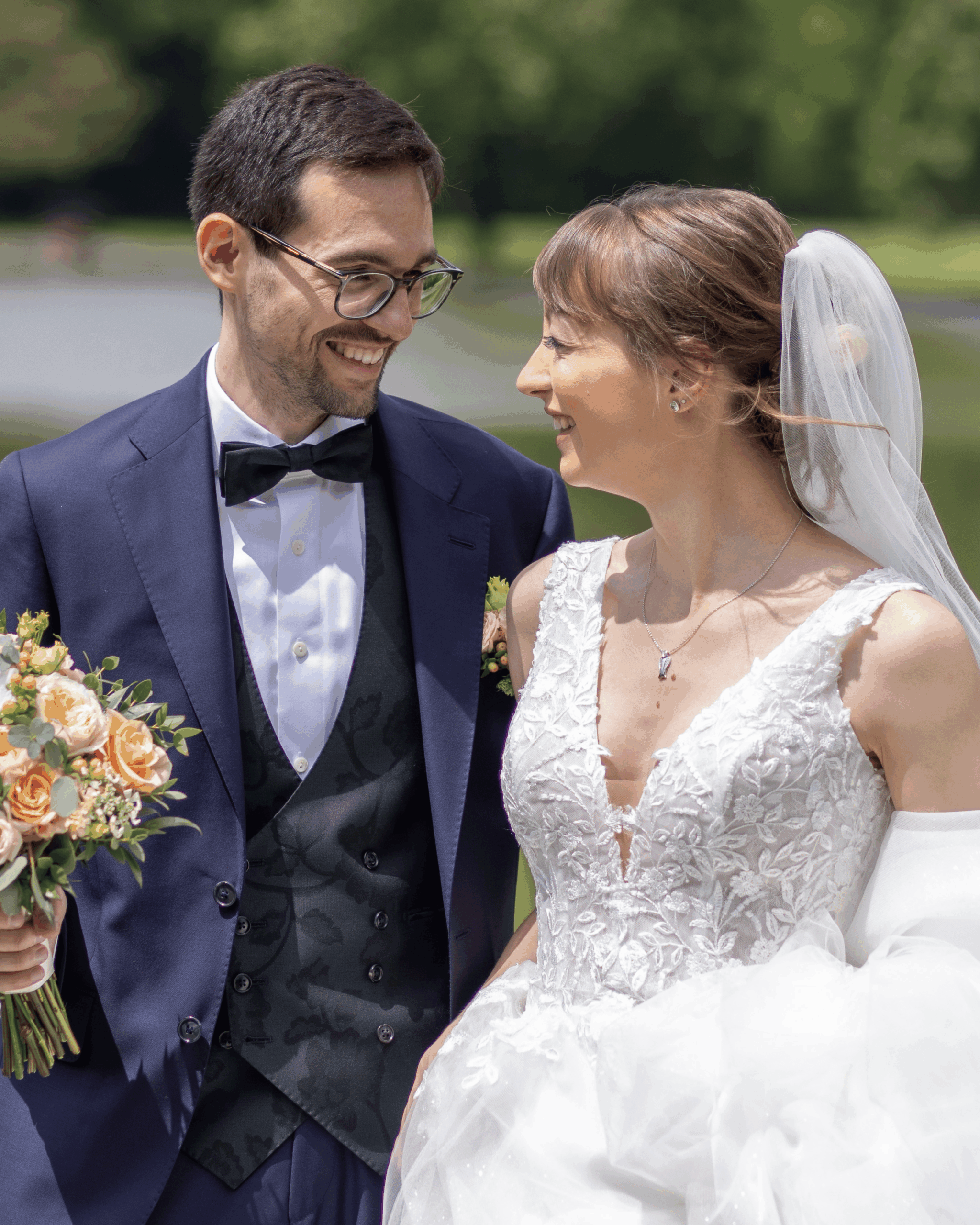 Lächelndes Brautpaar in eleganter Hochzeitskleidung blickt sich liebevoll an, Portrait im Freien